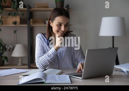 Smiling attractive young woman web surfing educational information online. Stock Photo