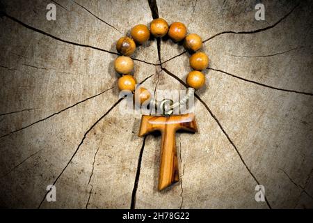 Tau, wooden cross in shape of the letter t (religious symbol of St. Francis of Assisi) with rosary bead. On a tree trunk section Stock Photo