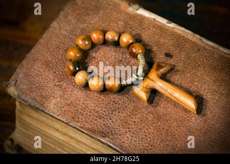 Tau, wooden cross in shape of the letter t (religious symbol of St. Francis of Assisi) with rosary bead on an old Holy Bible Stock Photo