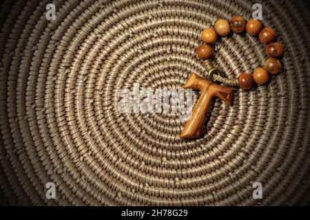 Tau, wooden cross in shape of the letter t (religious symbol of St. Francis of Assisi) with rosary bead, on brown woven wicker texture Stock Photo