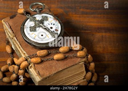 Time to Pray - Old pocket watch with a vintage silver crucifix and a rosary with wooden beads on an old Holy Bible Stock Photo