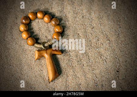 Tau, wooden cross in the shape of the letter t (religious symbol of St. Francis of Assisi) with rosary bead over the sand Stock Photo