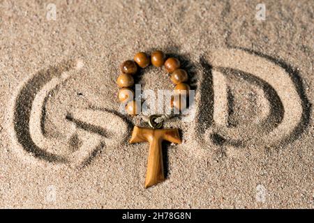 Tau, wooden cross in the shape of the letter t with rosary bead and the written God in the sand Stock Photo