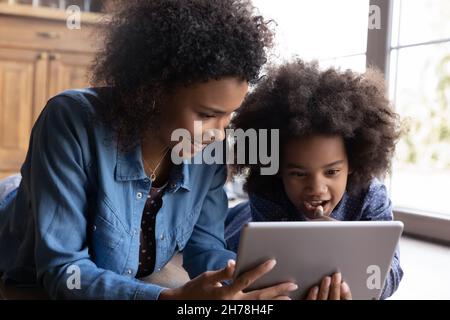 Caring smiling young African American mother using tablet with kid. Stock Photo