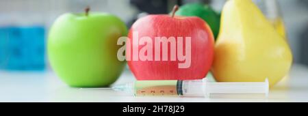 Apples and pear lying on table in laboratory near syringe with medicine closeup Stock Photo