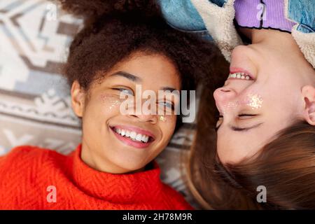 Female friendship. Two young diverse girlfriends of african american and caucasian ethnicity looking at each other with love while resting on plaid ou Stock Photo