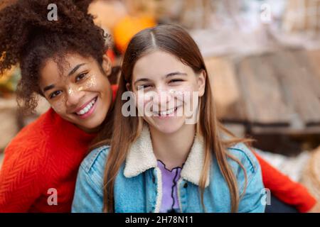 Portrait of two happy multiracial girlfriends smiling at camera while spending time in fall nature, cheerful teen girls of different races enjoying wa Stock Photo