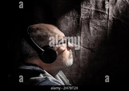 Low key profile portrait of a grey haired male listening to music through head phones Stock Photo