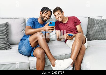 Two men friends using smartphone sitting on sofa at home Stock Photo