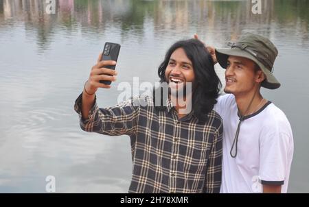 Two male friends having fun while taking selfie together in beside of lake Stock Photo