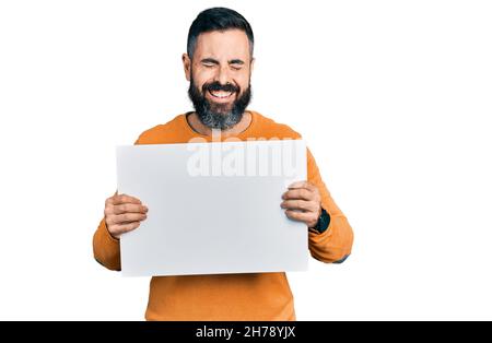 Hispanic man with beard holding blank empty banner smiling and laughing hard out loud because funny crazy joke. Stock Photo