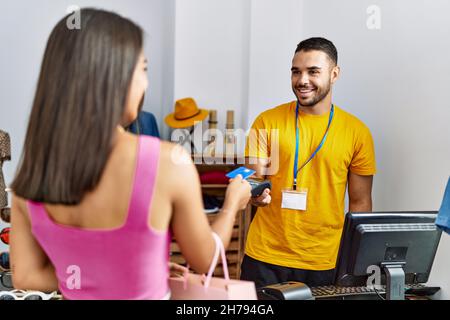 Young latin customer man paying to shopkeeper using credit card at clothing store. Stock Photo