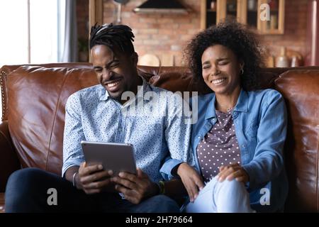 Joyful millennial African ethnicity family couple using digital tablet. Stock Photo