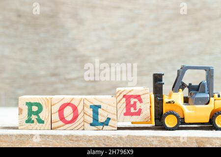Toy forklift hold letter block e to complete word role on wood background Stock Photo