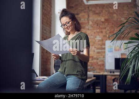 Busy interior designer or architect wearing glasses working on a blueprint for new project, leaning on the table in her office Stock Photo