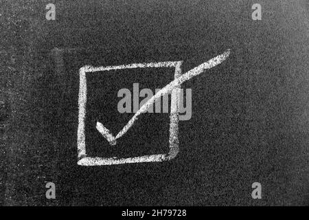 White color chalk hand drawing in right checkmark in square box shape on black board background Stock Photo
