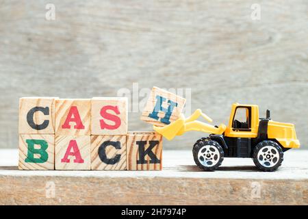 Toy bulldozer hold letter block H, K in word cash backon wood background Stock Photo