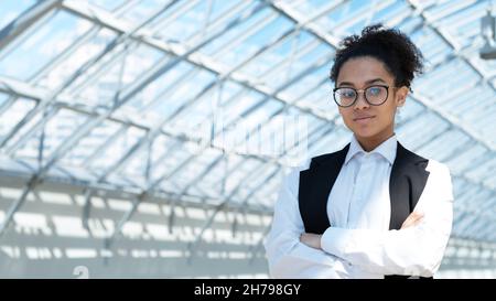 Close up portrait of young mixed race business woman standing with arms crossed in modern office Stock Photo