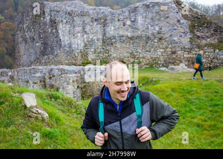 Portrait of a young smiling wanderer man with backpack goes on up the road happy hiker walking lonely Stock Photo