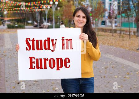 A woman smiles and holds a poster with the text Study in Europe Stock Photo