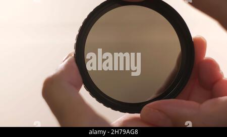 Photographic camera equipment filter isolated on white background. Female hands demonstrating the effect of polarizing filter for camera lens. Stock Photo