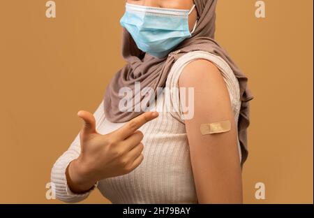 I got my covid-19 vaccine. Vaccinated muslim lady showing arm after vaccination and pointing at plaster, closeup, crop Stock Photo