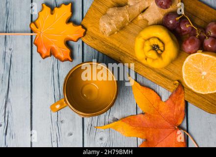 Autumn still life - bunch of grapes, ripe quince, ginger root, lemon lie on wooden table top view. Ginger cookies in shape of maple leaf, fallen leave Stock Photo