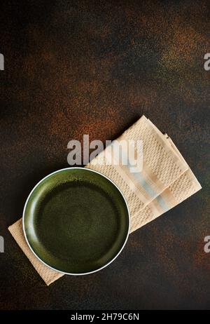 Empty green plate in grunge style on kitchen towel, top view, dark background Stock Photo