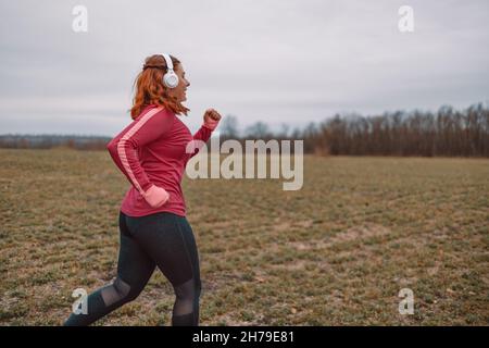 Active run woman with white headphones running in nature autimn fall. Fitness healthy lifestyle concept. Stock Photo