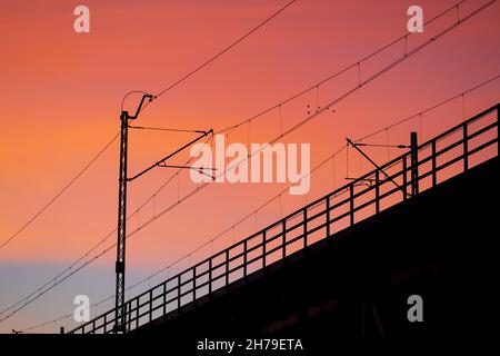 Sunset sky with silhouette of railway bridge electric traction and balustrade. Stock Photo