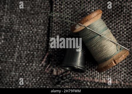 A retro needle with threads and an old thimble lie on a piece of cloth. Tailor and seamstress tools Stock Photo