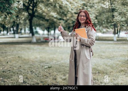 Portrait of female college student poses looking at camera showing thumb up in the street Stock Photo