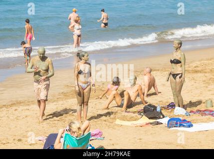 Gran Canaria, Canary Islands, Spain. 21st November, 2021. Tourists, many from the UK, bask in glorious sunshine on the city beach in Las Palmas on Gran Canaria; a popular winter sun destination for many British holidaymakers. PICTURED: Tourists enjoying a full body mud pack session on the city beach in Las Palmas. Credit: Alan Dawson/Alamy Live News. Stock Photo
