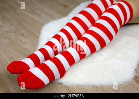 Girl in Christmas knee socks sitting on white fur rug on wooden floor. Female outfit for New Year celebration Stock Photo