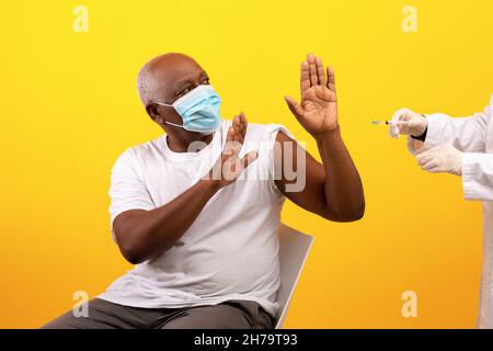 Senior African American male patient in face mask stopping doctor from making covid vaccine injection Stock Photo