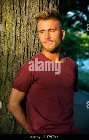 Sad, worried blond young man against tree Stock Photo