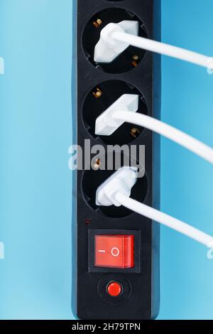 Surge protector with connected white wires of electrical appliances on a blue background. Free space Stock Photo