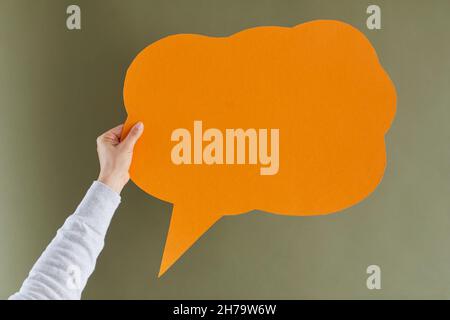 Woman's hand holding orange blank mockup paper speech balloon on green background Stock Photo