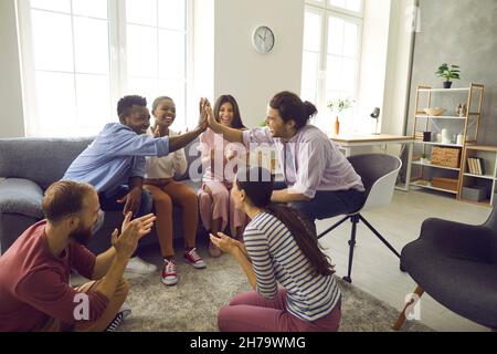 Two interracial men give five to each other while sitting in the company of friends at home. Stock Photo