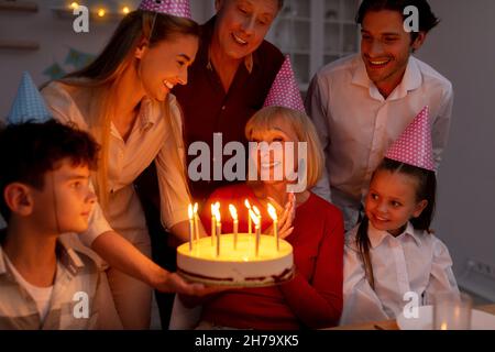 Happy multi generation family having birthday party, giving cake with candles to senior woman, celebrating holiday Stock Photo