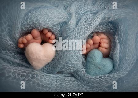 Newborn twins. Knitted hearts of blue and pink color in the legs of twins Stock Photo
