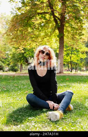 beautiful girl with fashion sunglasses sitting on the lawn looking at the camera Stock Photo