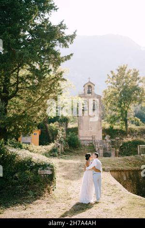 Bride and groom hugging and kissing near the ancient bell tower near the church in Prcanj, back view Stock Photo