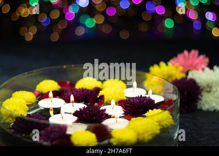 Floating Tealight Candles Illuminated In Decorative Urli Crystal Bowl Filled With Water And Flowers. Colorful Bokeh On Dark Background. Theme For Shub Stock Photo