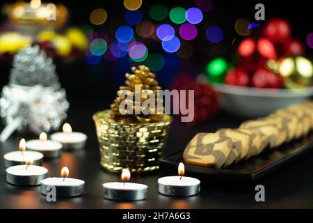 Decorative Tealight Candles With Pine Cones Cookies Food Baubles And Colorful Bokeh On Dark Background. Theme For Merry Christmas And Happy New Year Stock Photo