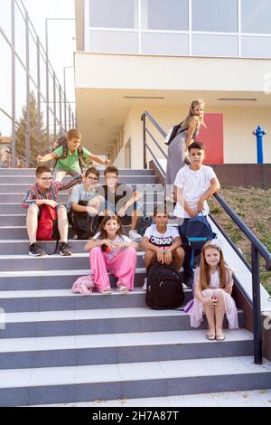 Group of elementary school kids having fun before classes, sitting on the stairs. Back to school Stock Photo
