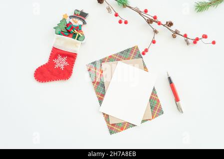 Christmas blank greeting card mock-up scene. Christmas decoration composition on white background with blank greeting card and envelope, fir branch, p Stock Photo