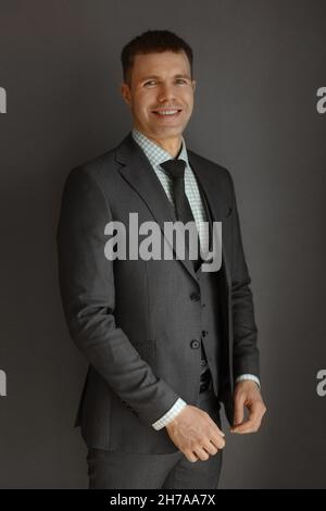 A handsome guy in a trendy grey suit, checkered shirt, and tie posing over grey background. Young handsome businessman in formal clothes smiling and Stock Photo