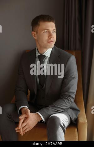 Fashionable young man wearing suit in the interior. Handsome young model in a classic style suit posing in an armchair Stock Photo