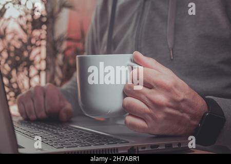 Freelancer is drinking coffee and working from home on laptop computer, selective focus Stock Photo
